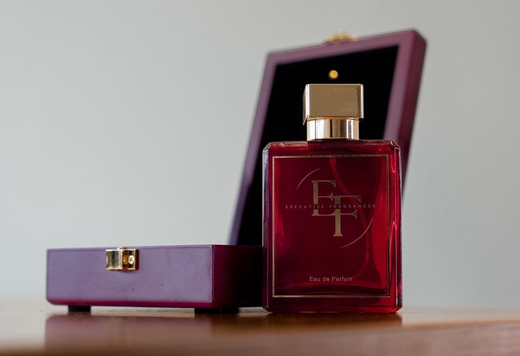 Red perfume bottle with gold cap on a wooden surface next to an ope red box.